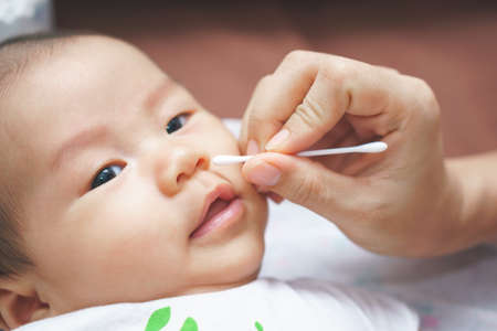 Mother hand cleaning baby ear and nose with cotton swabの写真素材