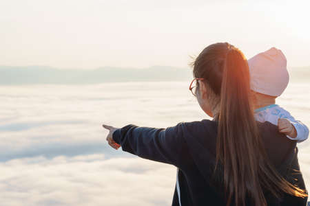 Asian Mother pointing her baby to see the fog over mountainの写真素材