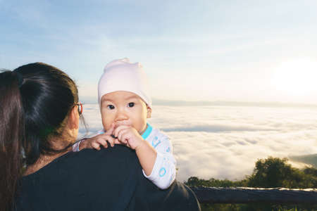 Asian Mother holding her baby to see the fog over mountainの写真素材