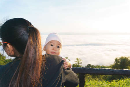 Asian Mother holding her baby to see the fog over mountainの写真素材