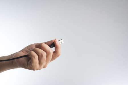 Hand holding black USB cable on white backgroundの写真素材