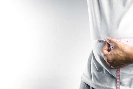 Man measuring his fat belly with measurement tapeの写真素材