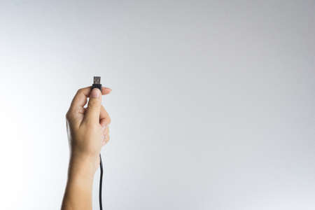 Hand holding black USB cable on white backgroundの写真素材