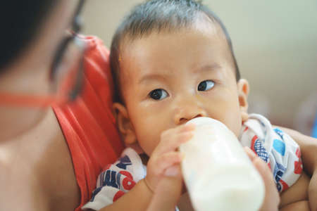 Crying Asian kid drinking breastfeeding milk from bottle after eating foodの写真素材