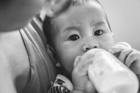 Crying Asian kid drinking breastfeeding milk from bottle after eating foodの写真素材