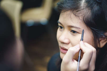 Makeup artist applies eyebrow on Asian woman faceの写真素材