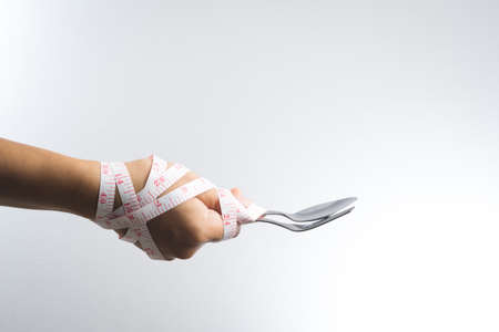 Man hand holding a silver fork and spoon with measuring tape for diet conceptの写真素材