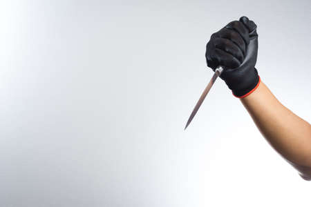 Hand with black grove holding a knife on white backgroundの写真素材