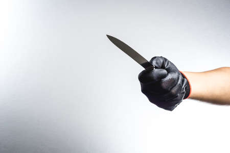 Hand with black grove holding a knife on white background