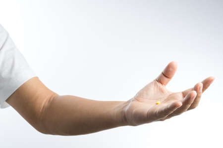 Hand with yellow pill in palm on white backgroundの写真素材