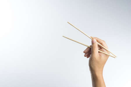 Hand holding disposable wooden chopsticks made of bamboo on white backgroundの写真素材