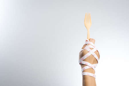 Man hand holding a wooden fork and spoon with measuring tape for diet conceptの写真素材