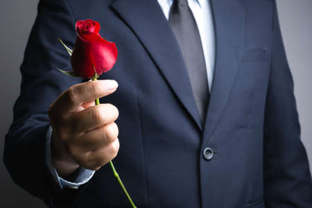 Business man hand with red rose flower on white backgroundの写真素材