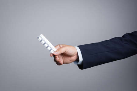 Business man hand holding white medicine pills in blister pack on white backgroundの写真素材
