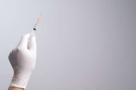 Hand wearing latex glove holding syringe with a medicine on white backgroundの写真素材