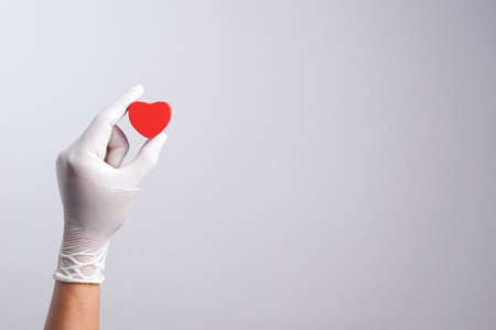 Hand wearing latex glove holding wooden heart shape object on white backgroundの写真素材