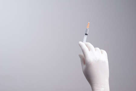 Hand wearing latex glove holding syringe with a medicine on white backgroundの写真素材