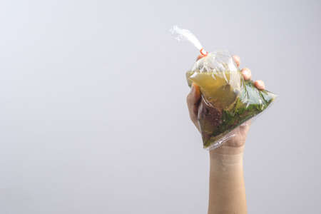 Hand holding boiled pig's blood soup with peppers in plastic bag wrapped by rubber band, An ordinary...