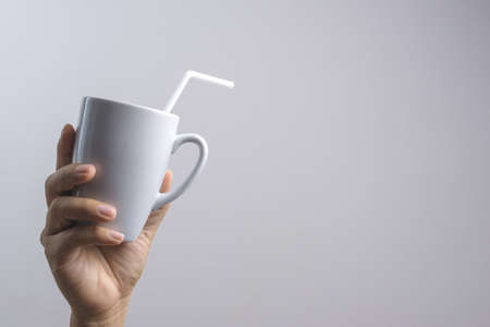 Hand holding mug with a straw on white background