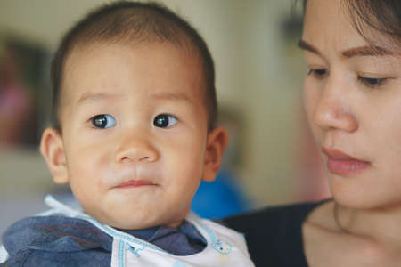 Asian Mother holding her 10 months son with serious expression