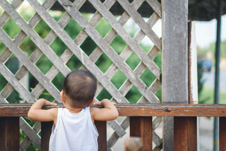 Asian baby waiting for parent at house wooden fenceの写真素材