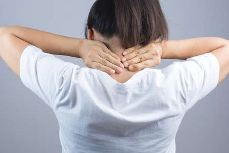 Woman putting her hand for neck or spine pain on grey backgroundの写真素材