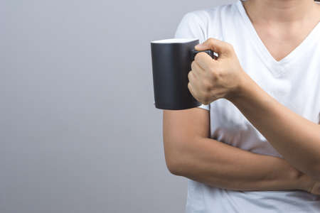 Woman hand holding black mug on grey background
