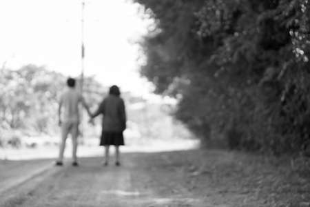 Lens blurred back view of young Asian couple holding hands at the parkの写真素材