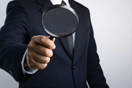 Business man hand holding magnifier for inspection on white backgroundの写真素材