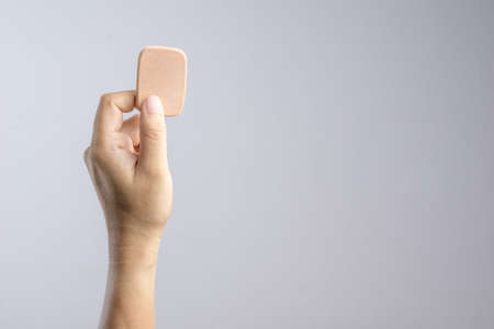 Hand holding brown face sponge for cosmetics on white backgroundの写真素材