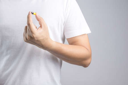 Hand holding medical capsule pill on white backgroundの写真素材