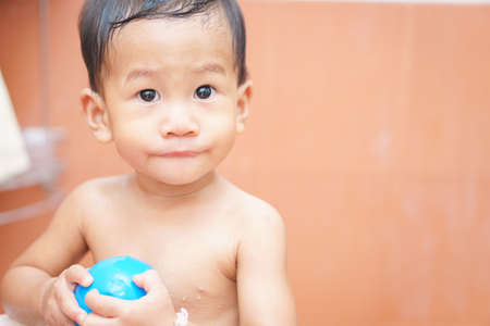 A year old and 5 months Asian baby play a ball while taking a shower by himselfの写真素材