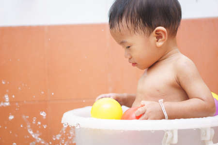 A year old and 5 months Asian baby play a ball while taking a shower by himselfの写真素材
