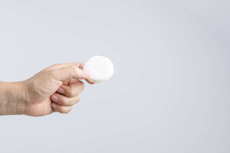 Hand holding round common hotel soap wrapped by paper on white background