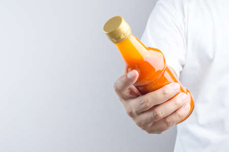 Hand holding spicy red hot sauce in glass bottle for Sukiyaki or hot pot on white backgroundの写真素材