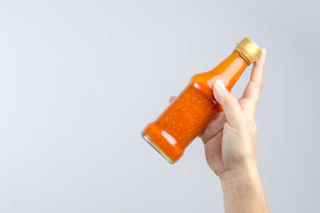 Hand holding spicy red hot sauce in glass bottle for Sukiyaki or hot pot on white backgroundの写真素材
