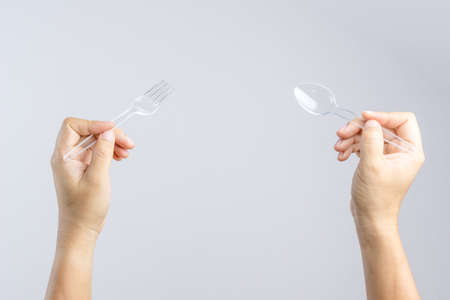 Hand holding plastic spoon and fork on white backgroundの写真素材