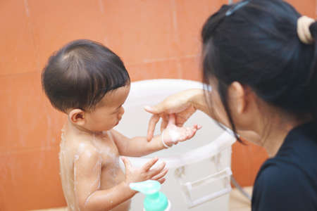 Asian mother teach her one year old and 5 months baby to take a shower by himselfの写真素材