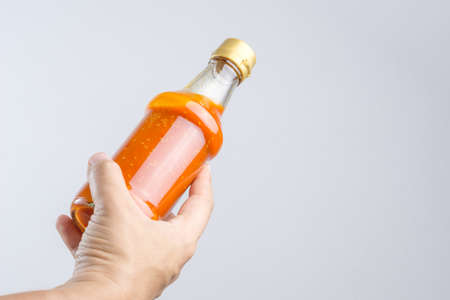 Hand holding spicy red hot sauce in glass bottle for Sukiyaki or hot pot on white backgroundの写真素材