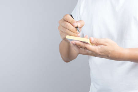 Hand holding sticky post note paper sheet with writing pen gesture on white backgroundのeditorial素材