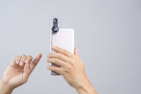 Hand holding smart phone equipped with extension lens on white backgroundのeditorial素材