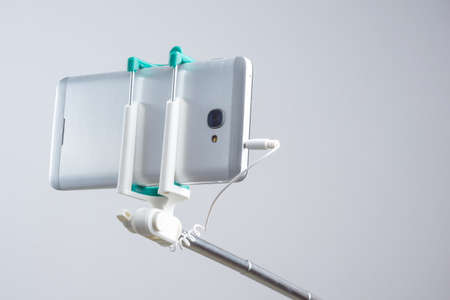 Extensible selfie stick connected to smart phone on white background