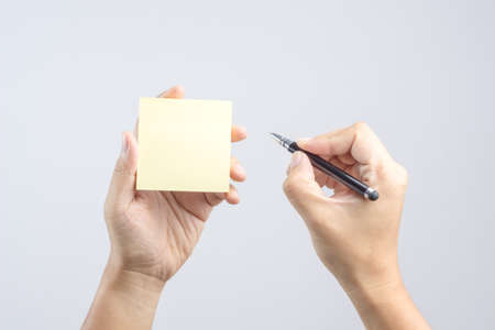 Hand holding sticky post note paper sheet with writing pen gesture on white backgroundのeditorial素材