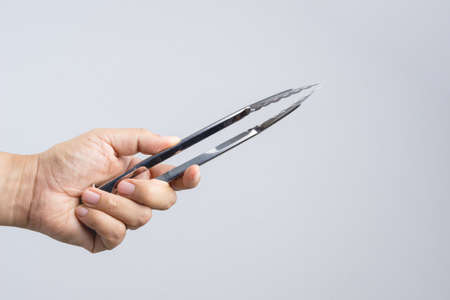 Hand holding silver serving kitchen tongs for picking food on white backgroundのeditorial素材