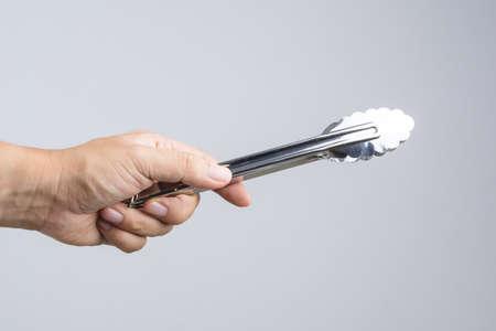 Hand holding silver serving kitchen tongs for picking food on white backgroundのeditorial素材