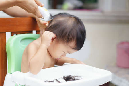 A year and sixth months old Asian baby got hair cut by his mother using electric hair clipperの写真素材