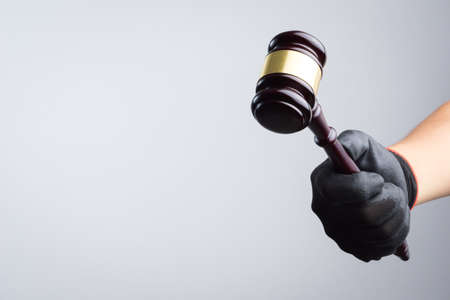 Hand wearing black glove holding wooden judge's gavel as a illegal or injustice sign on white...