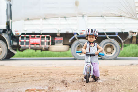 Asian boy about 1 year and 6 months is playing with baby balance bike near rural street while car passing by as a dangerous and accident for kid conceptの写真素材