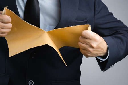 Business man hand tearing self sealing brown envelope document in anger on white backgroundのeditorial素材