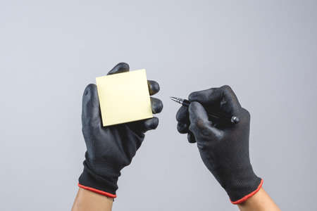 Hand wearing dark glove and holding pen and sticky paper note as a person who do something bad like blackmail on white backgroundのeditorial素材